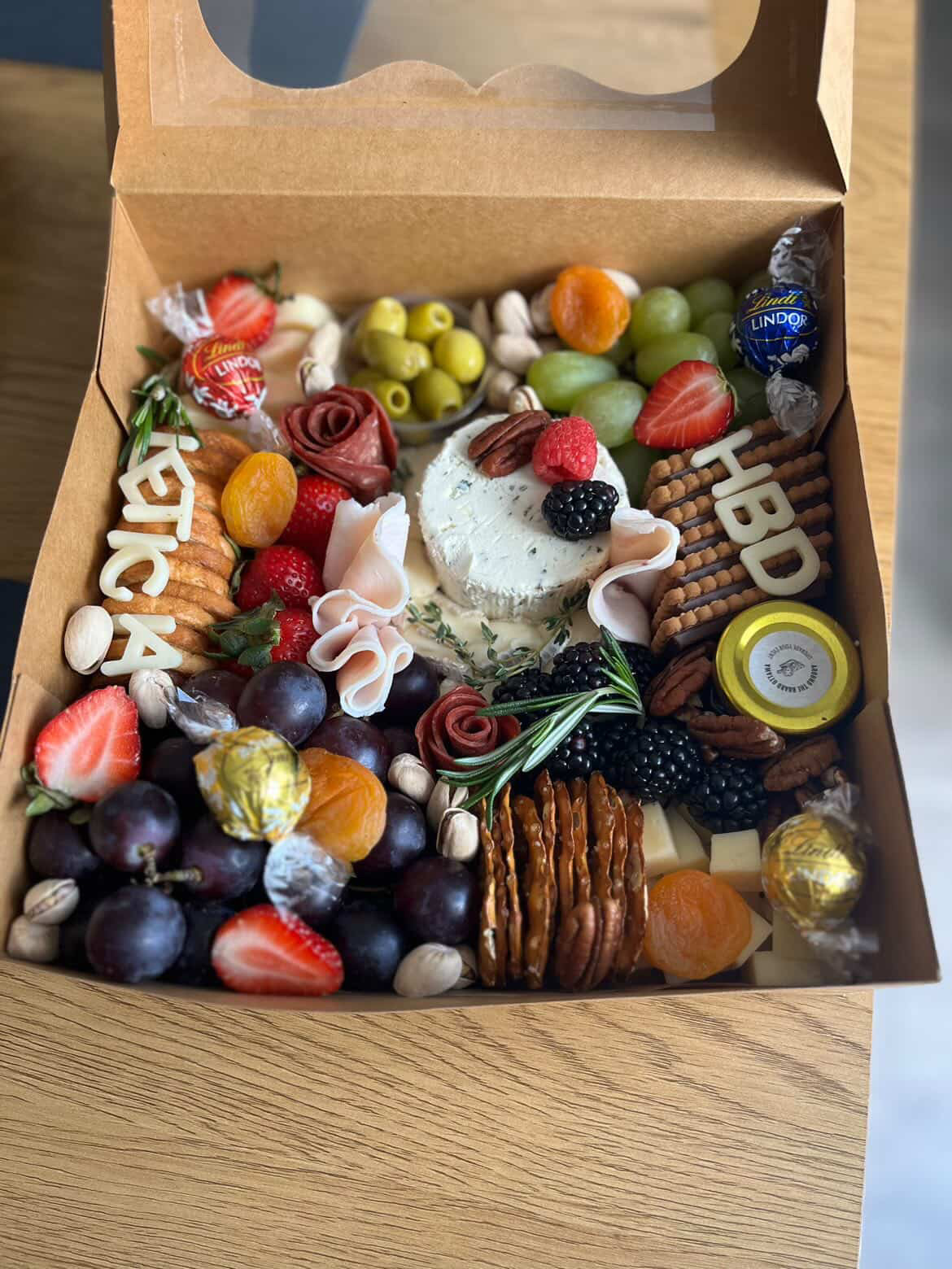 Open large grazing box with artisan cheeses, cured meats and grapes